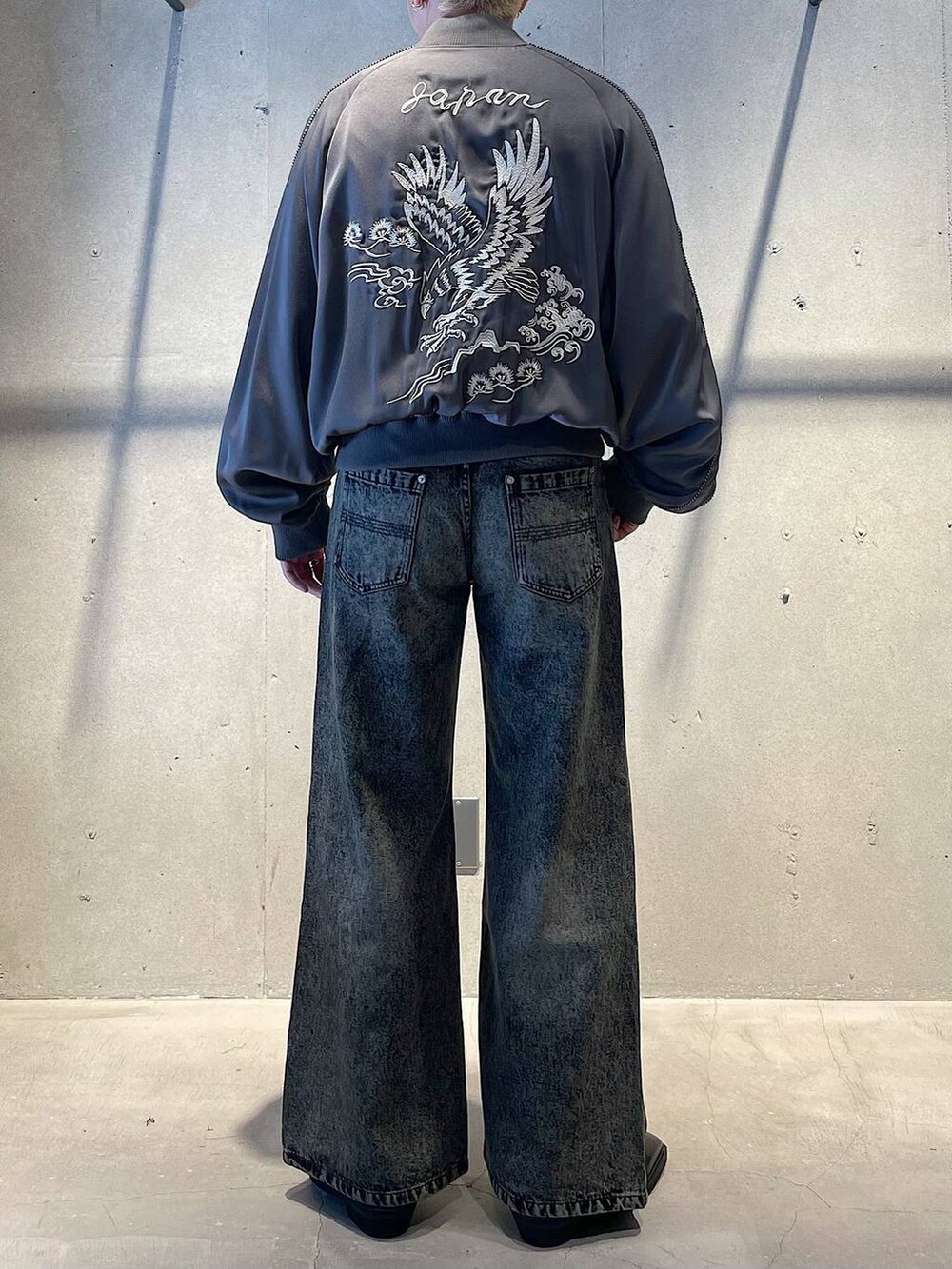 グリーン系のデニムパンツ、グレー系のスカジャン、ブラック系のブーツを着用したメンズの秋コーディネートの2枚目の写真