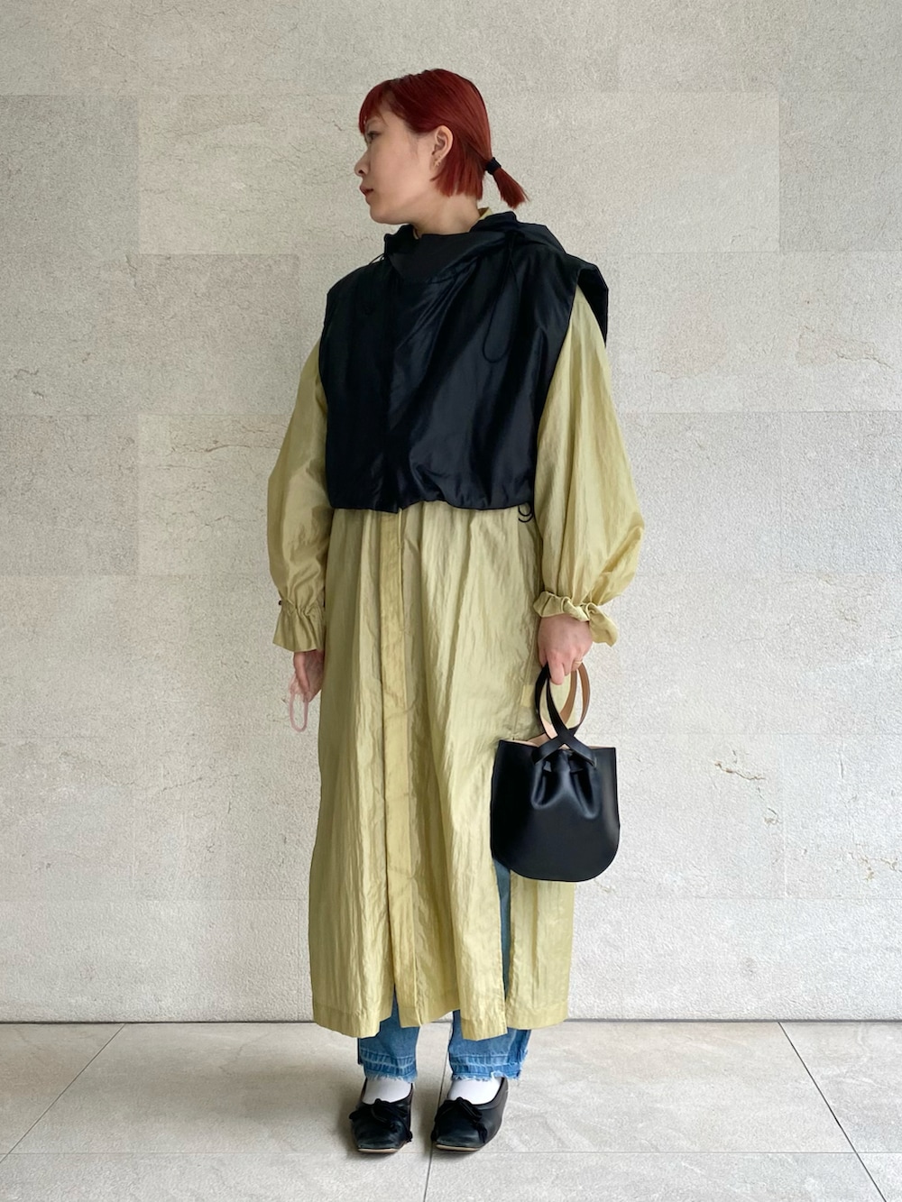 ブラック系のハンドバッグ、ブラック系のベスト、イエロー系のシャツワンピースを着用したレディースの春コーディネートの2枚目の写真