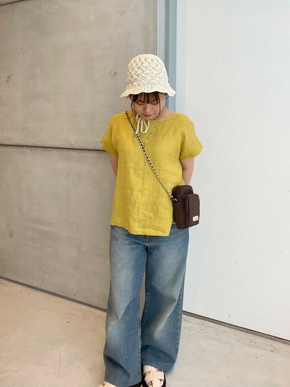 ブルー系のデニムパンツ、ホワイト系のサンダル、ブラウン系のショルダーバッグを着用したレディースの夏コーディネートの2枚目の写真