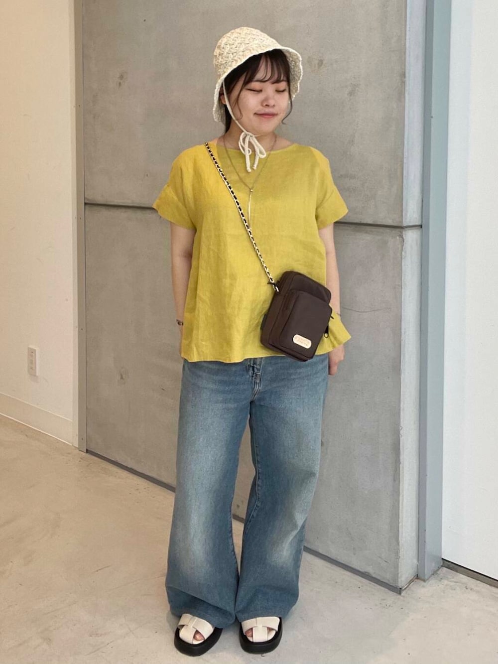 ブルー系のデニムパンツ、ホワイト系のサンダル、ブラウン系のショルダーバッグを着用したレディースの夏コーディネートの3枚目の写真