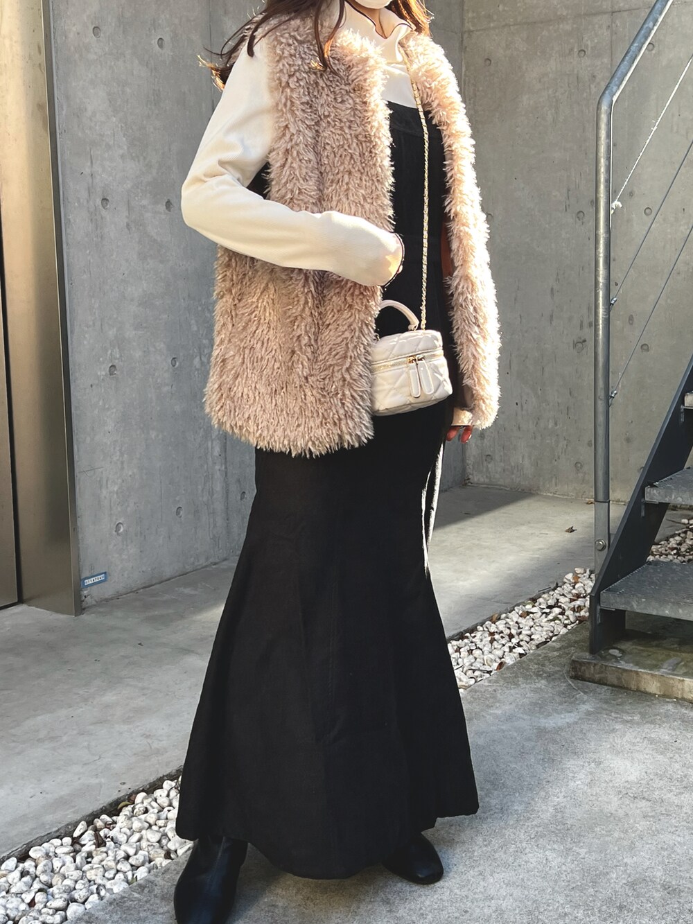 ベージュ系のベスト、ブラック系のワンピース、ホワイト系のショルダーバッグを着用したレディースの冬コーディネートの2枚目の写真