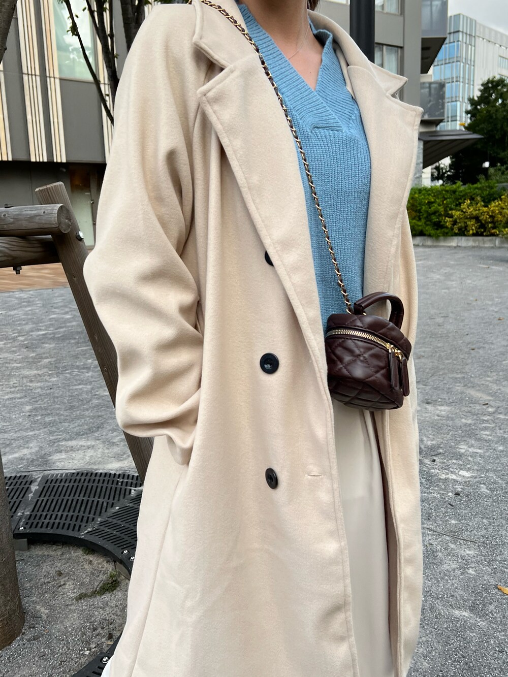 ブラック系のチェスターコート、ブルー系のニット/セーター、ホワイト系のワンピースを着用したレディースの冬コーディネートの2枚目の写真