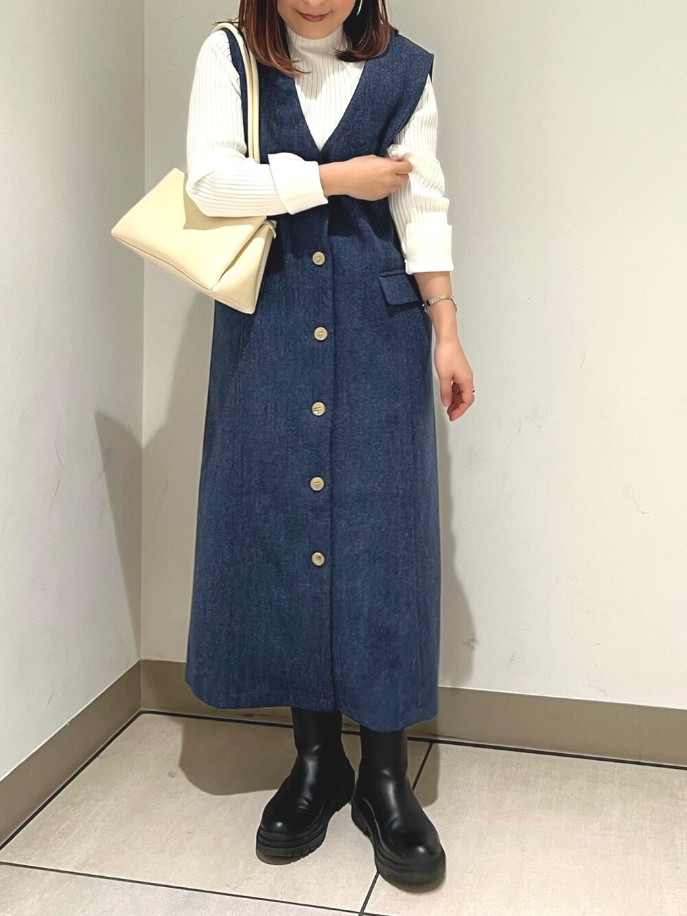 ブルー系のジャンパースカート、ホワイト系のニット/セーター、ホワイト系のショルダーバッグを着用したレディースの冬コーディネートの2枚目の写真