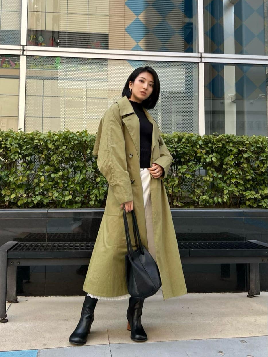 ブラック系のニット/セーター、ブラック系のブーツ、グリーン系のトレンチコートを着用したレディースの春コーディネートの2枚目の写真