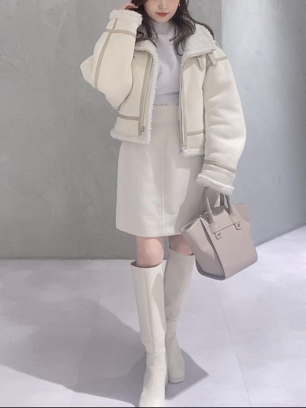 ベージュ系のハンドバッグ、ホワイト系のムートンコート、パープル系のニット/セーターを着用したレディースの冬コーディネートの2枚目の写真