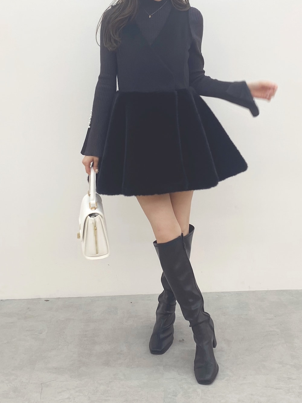ブラック系のブーツ、ブラック系のワンピース、ホワイト系のハンドバッグを着用したレディースの秋コーディネートの3枚目の写真
