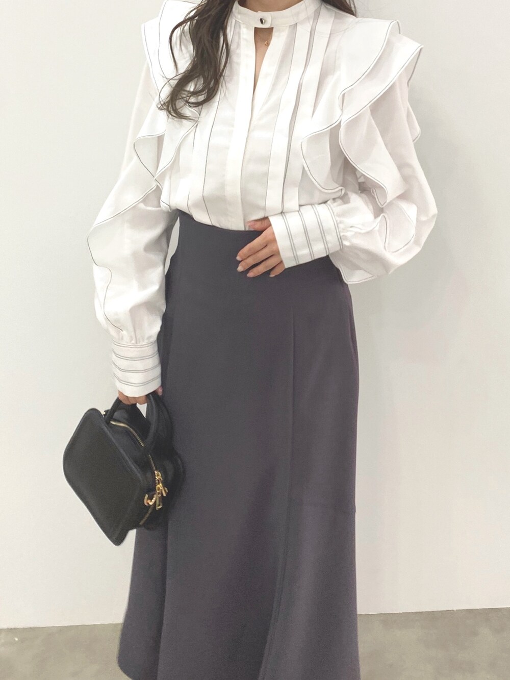グレー系のスカート、ホワイト系のシャツ/ブラウス、ブラック系のハンドバッグを着用したレディースの冬コーディネートの3枚目の写真