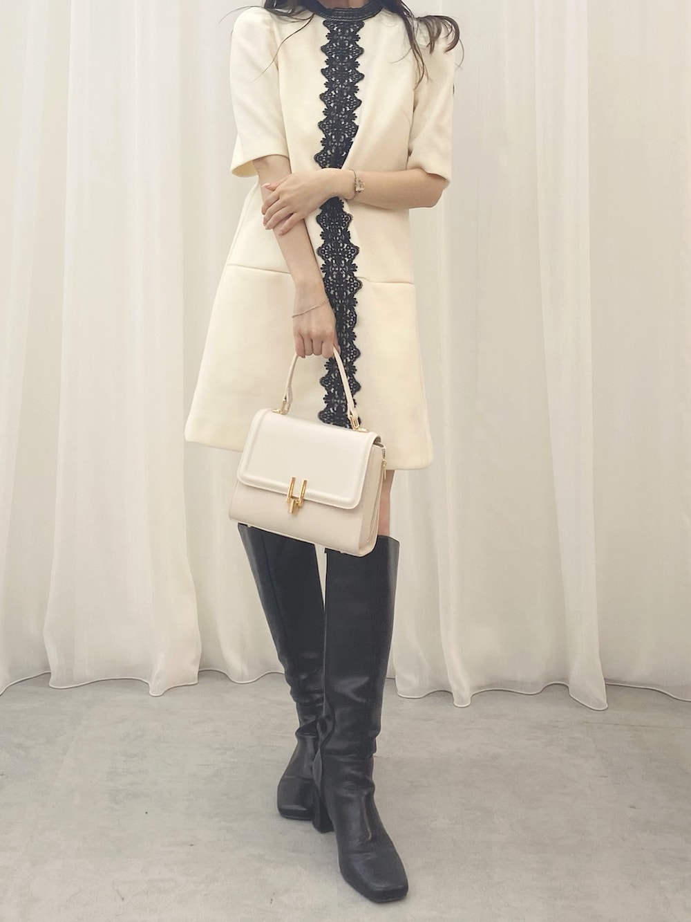 ホワイト系のハンドバッグ、ホワイト系のワンピース、ブラック系のブーツを着用したレディースの夏コーディネートの3枚目の写真