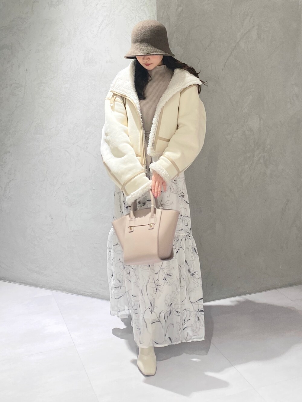ホワイト系のムートンコート、ホワイト系のブーツ、ベージュ系のハンドバッグを着用したレディースの冬コーディネートの2枚目の写真