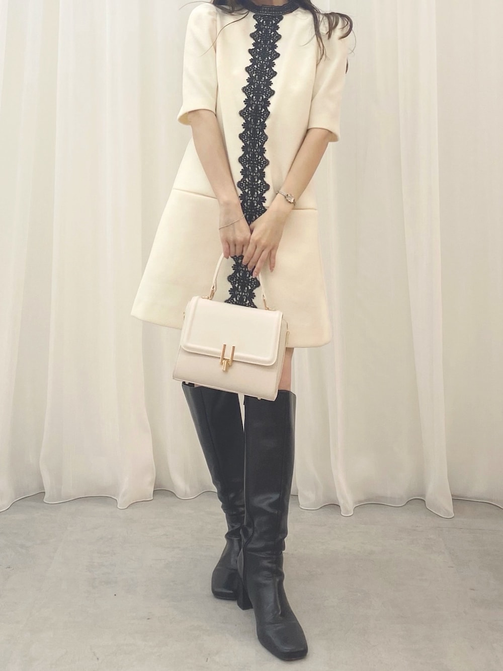 ホワイト系のハンドバッグ、ホワイト系のワンピース、ブラック系のブーツを着用したレディースの夏コーディネートの2枚目の写真