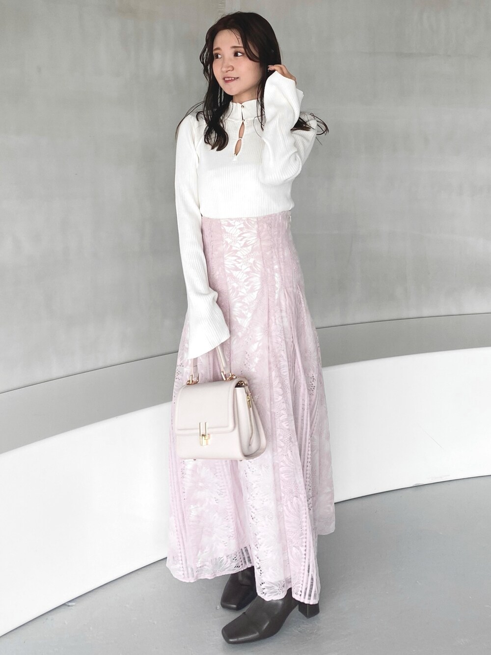 ピンク系のハンドバッグ、ピンク系のスカート、ホワイト系のニット/セーターを着用したレディースの冬コーディネートの3枚目の写真