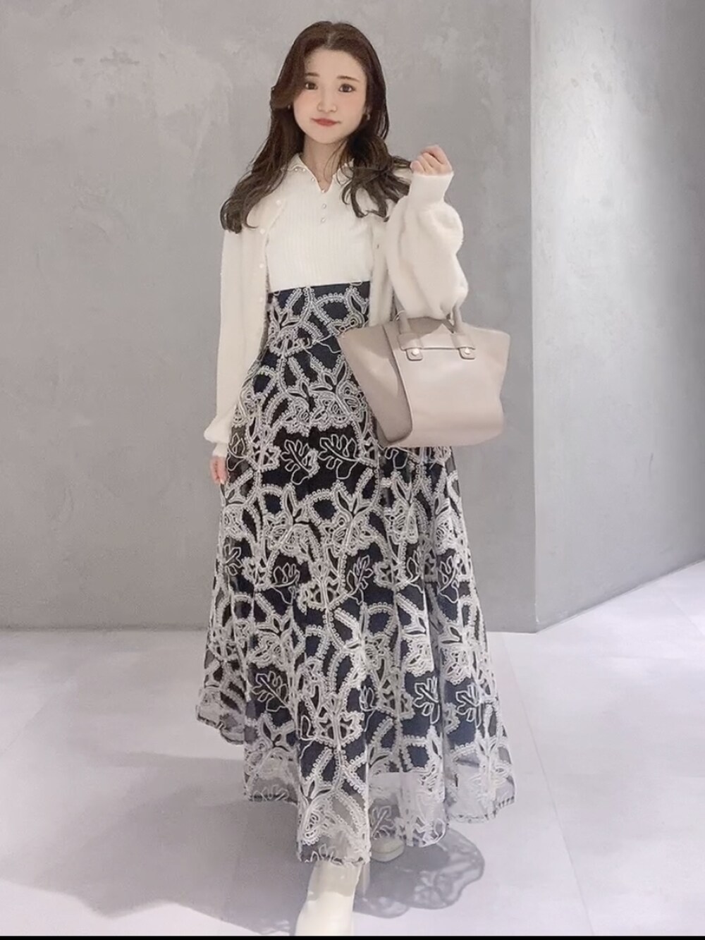 ベージュ系のハンドバッグ、ブラック系のスカート、ホワイト系のニット/セーターを着用したレディースの冬コーディネートの2枚目の写真