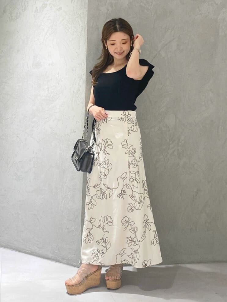 ブラック系のショルダーバッグ、ブラック系のニット/セーター、ホワイト系のスカートを着用したレディースの夏コーディネートの2枚目の写真