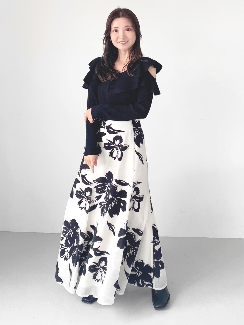 ブラック系のブーツ、ホワイト系のスカート、ブラック系のニット/セーターを着用したレディースの秋コーディネートの2枚目の写真