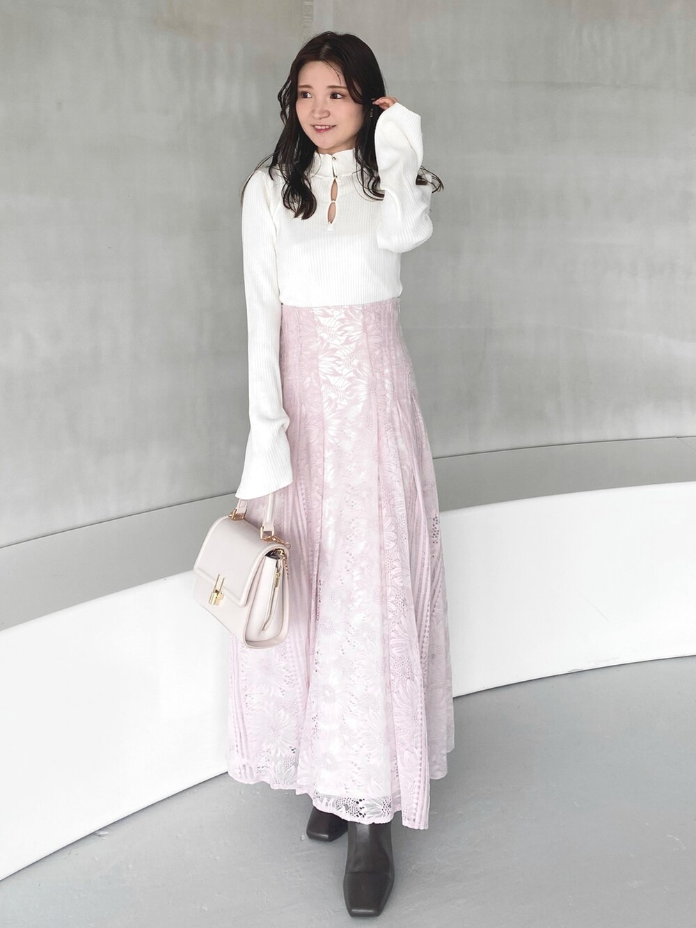 ピンク系のハンドバッグ、ピンク系のスカート、ホワイト系のニット/セーターを着用したレディースの冬コーディネートの2枚目の写真