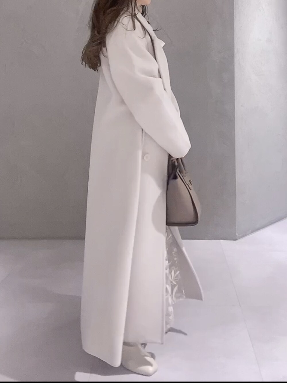 ホワイト系のニット/セーター、ホワイト系のチェスターコート、ブラウン系のハンドバッグを着用したレディースの冬コーディネートの3枚目の写真