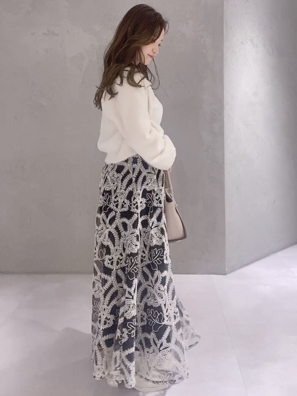 ベージュ系のハンドバッグ、ブラック系のスカート、ホワイト系のニット/セーターを着用したレディースの冬コーディネートの3枚目の写真