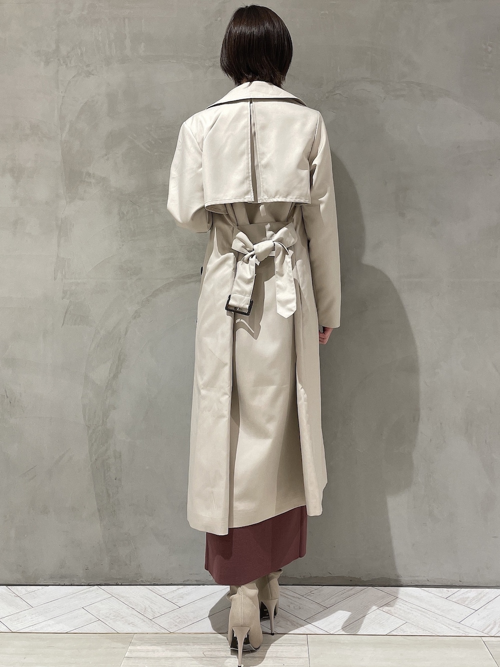 ベージュ系のトレンチコート、ブラウン系のワンピース、ホワイト系のブーツを着用したレディースの冬コーディネートの4枚目の写真