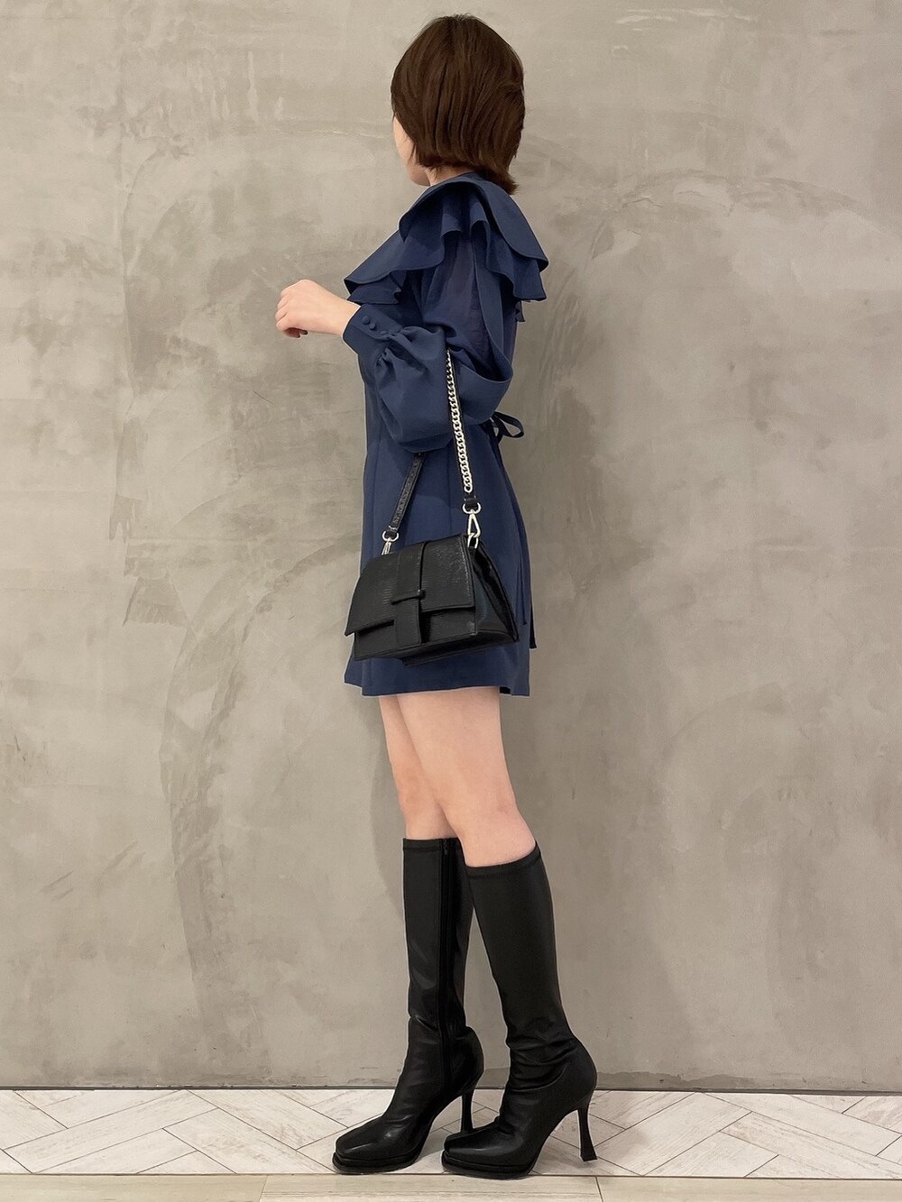 ブラック系のハンドバッグ、ブラック系のブーツ、ブルー系のワンピースを着用したレディースの冬コーディネートの2枚目の写真