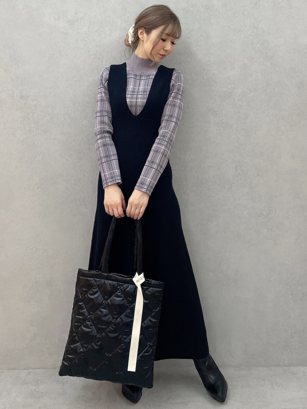 パープル系のニット/セーター、ブラック系のブーツ、ブラック系のジャンパースカートを着用したレディースの秋コーディネートの2枚目の写真