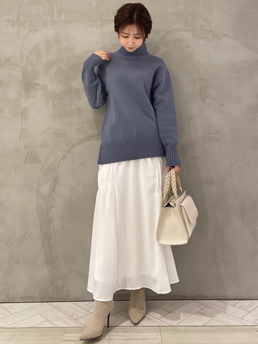 ホワイト系のブーツ、ホワイト系のハンドバッグ、ブルー系のニット/セーターを着用したレディースの冬コーディネートの2枚目の写真