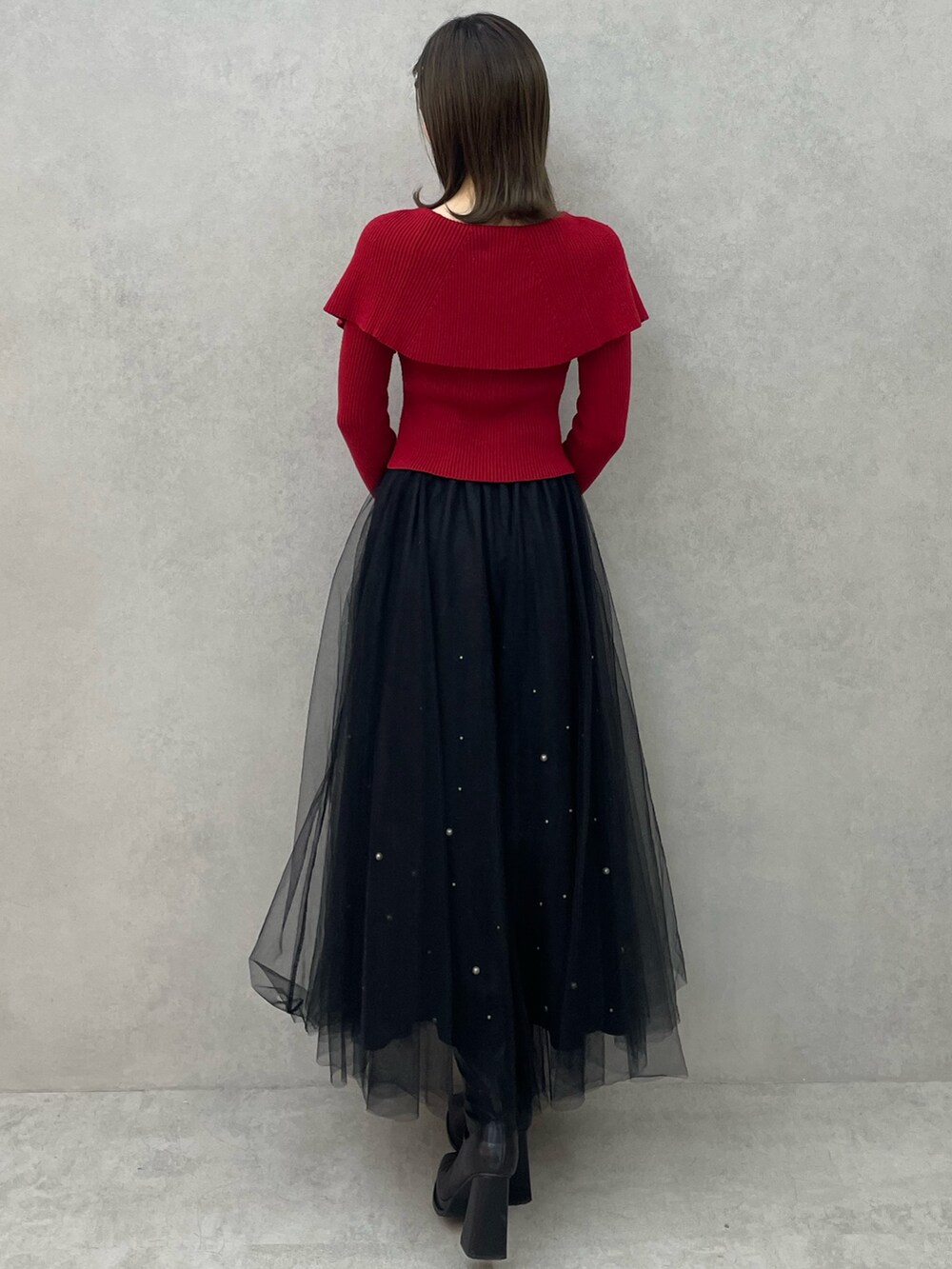 レッド系のニット/セーター、ブラック系のスカート、ブラック系のブーツを着用したレディースの秋コーディネートの5枚目の写真