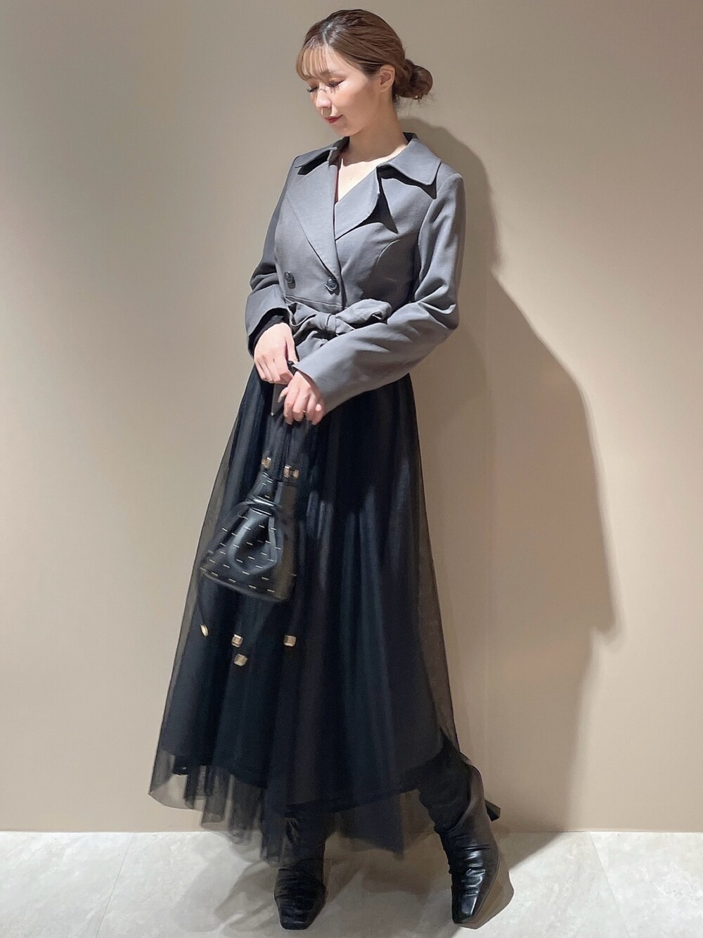 グレー系のトレンチコート、ブラック系のハンドバッグ、ブラック系のブーツを着用したレディースの秋コーディネートの2枚目の写真