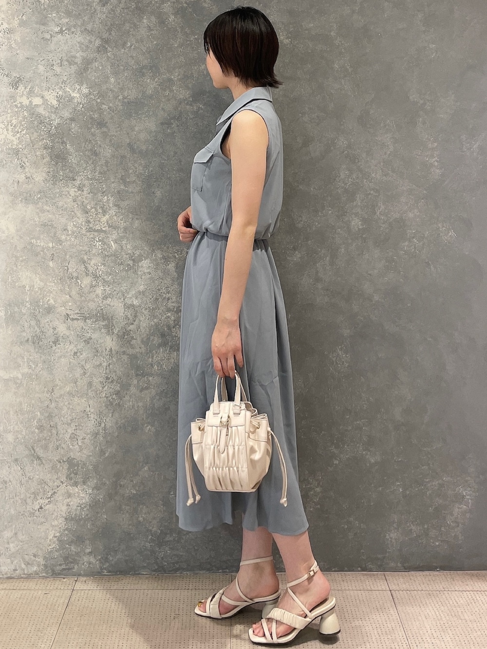 ホワイト系のハンドバッグ、ホワイト系のサンダル、ブルー系のシャツワンピースを着用したレディースの夏コーディネートの2枚目の写真