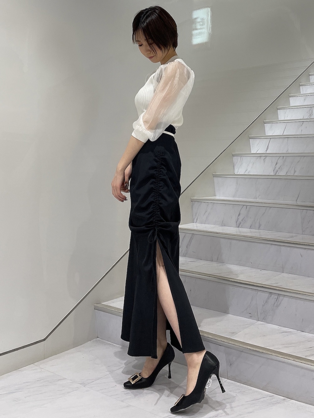 ホワイト系のニット/セーター、ブラック系のスカート、ブラック系のパンプスを着用したレディースの春コーディネートの2枚目の写真