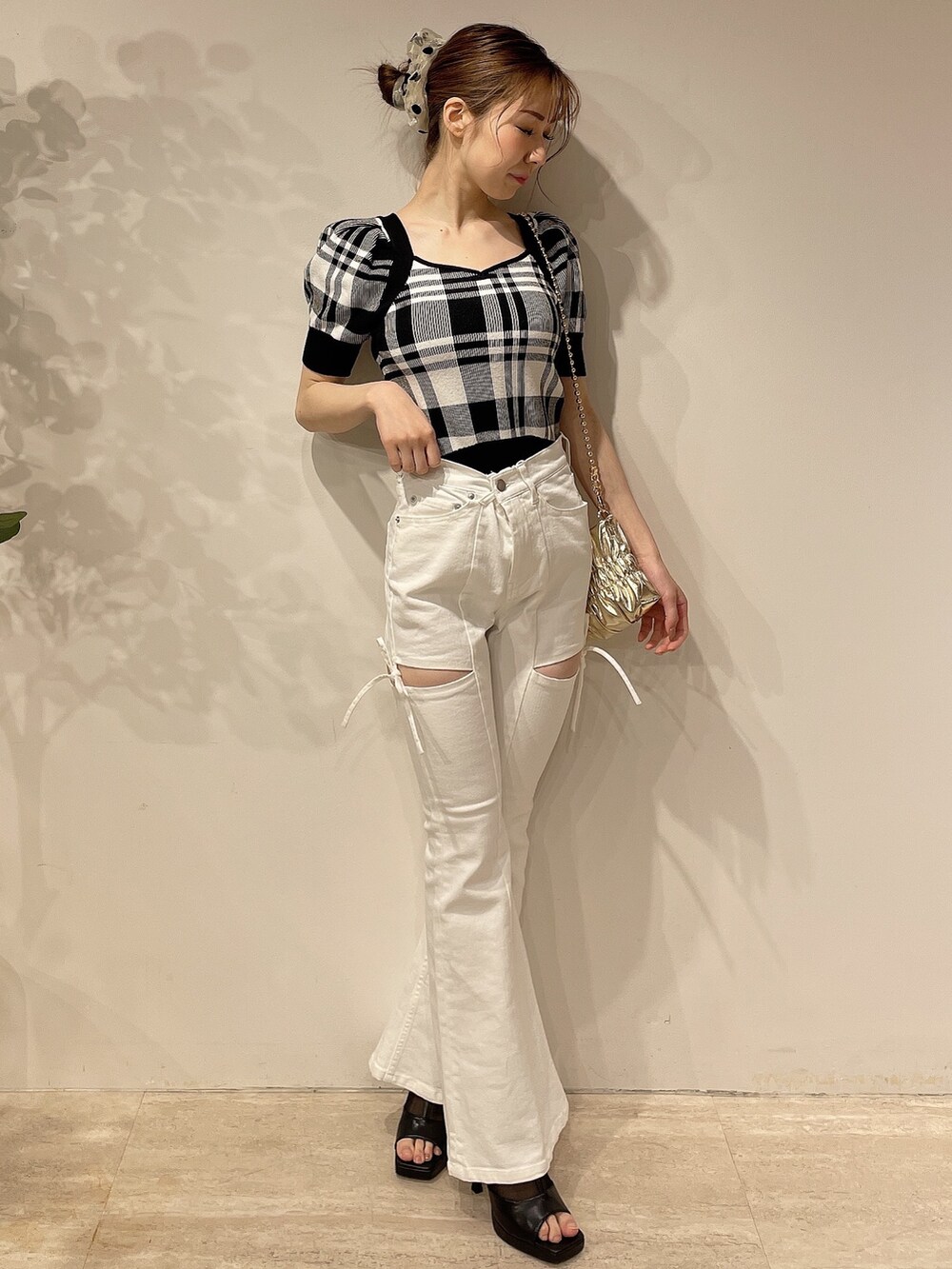 ブラック系のニット/セーター、ホワイト系のデニムパンツ、ゴールド系のハンドバッグを着用したレディースの春コーディネートの2枚目の写真