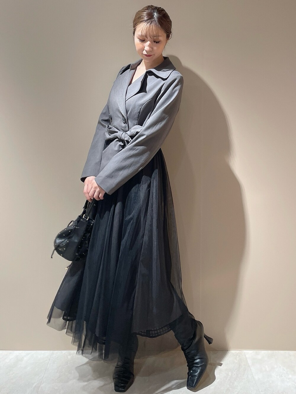 グレー系のトレンチコート、ブラック系のハンドバッグ、ブラック系のブーツを着用したレディースの秋コーディネートの3枚目の写真