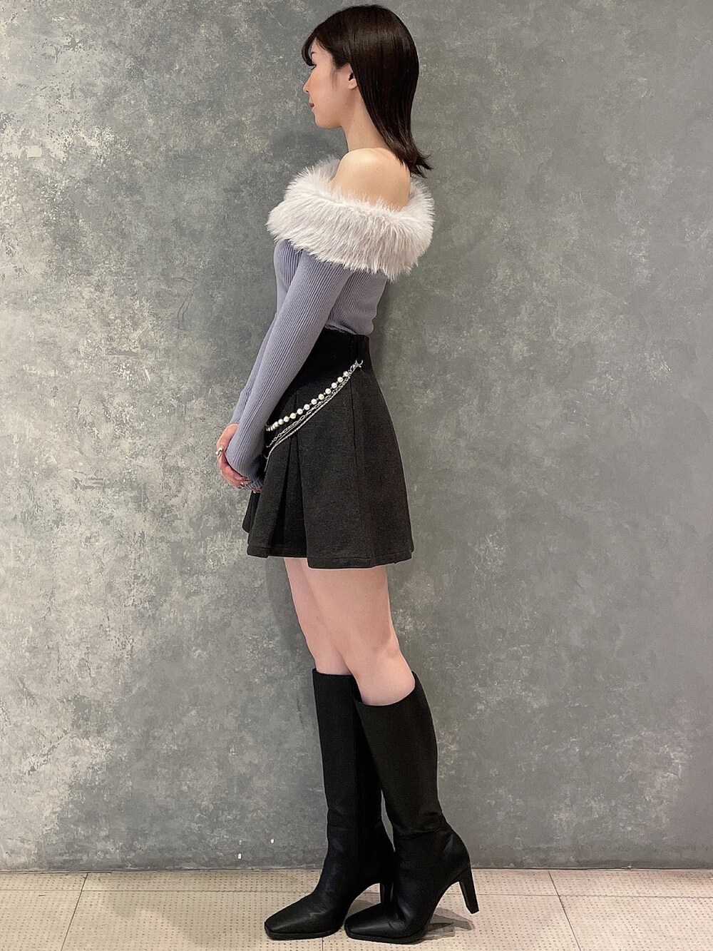 ブルー系のニット/セーター、グレー系のスカート、ブラック系のブーツを着用したレディースの秋コーディネートの2枚目の写真