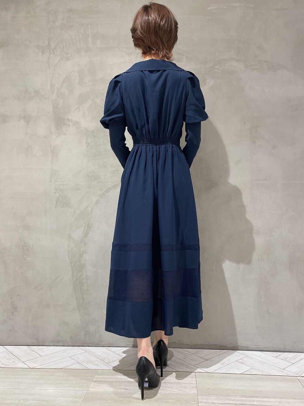 ブラック系のハンドバッグ、ブルー系のワンピース、ブラック系のパンプスを着用したレディースの冬コーディネートの4枚目の写真