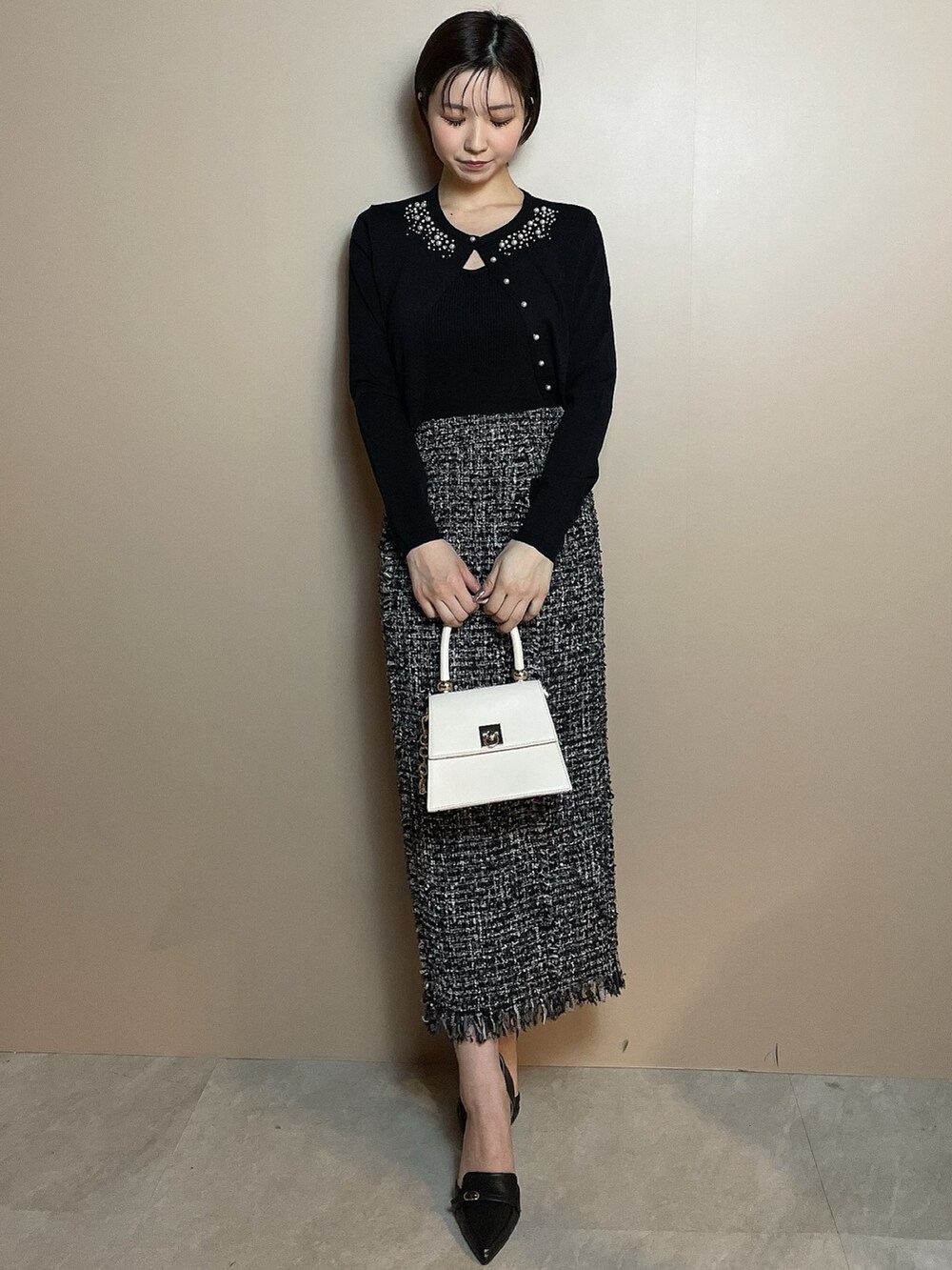 ホワイト系のハンドバッグ、ブラック系のカーディガン/ボレロ、ブラック系のスカートを着用したレディースの冬コーディネートの2枚目の写真