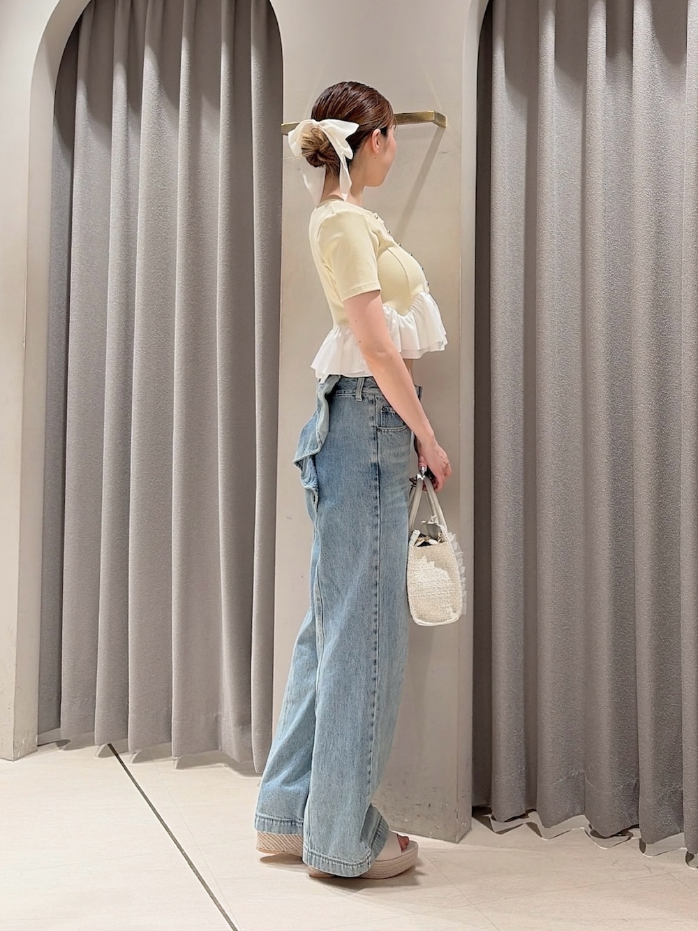 イエロー系のカーディガン/ボレロ、ホワイト系のトートバッグ、ブルー系のデニムパンツを着用したレディースの夏コーディネートの2枚目の写真