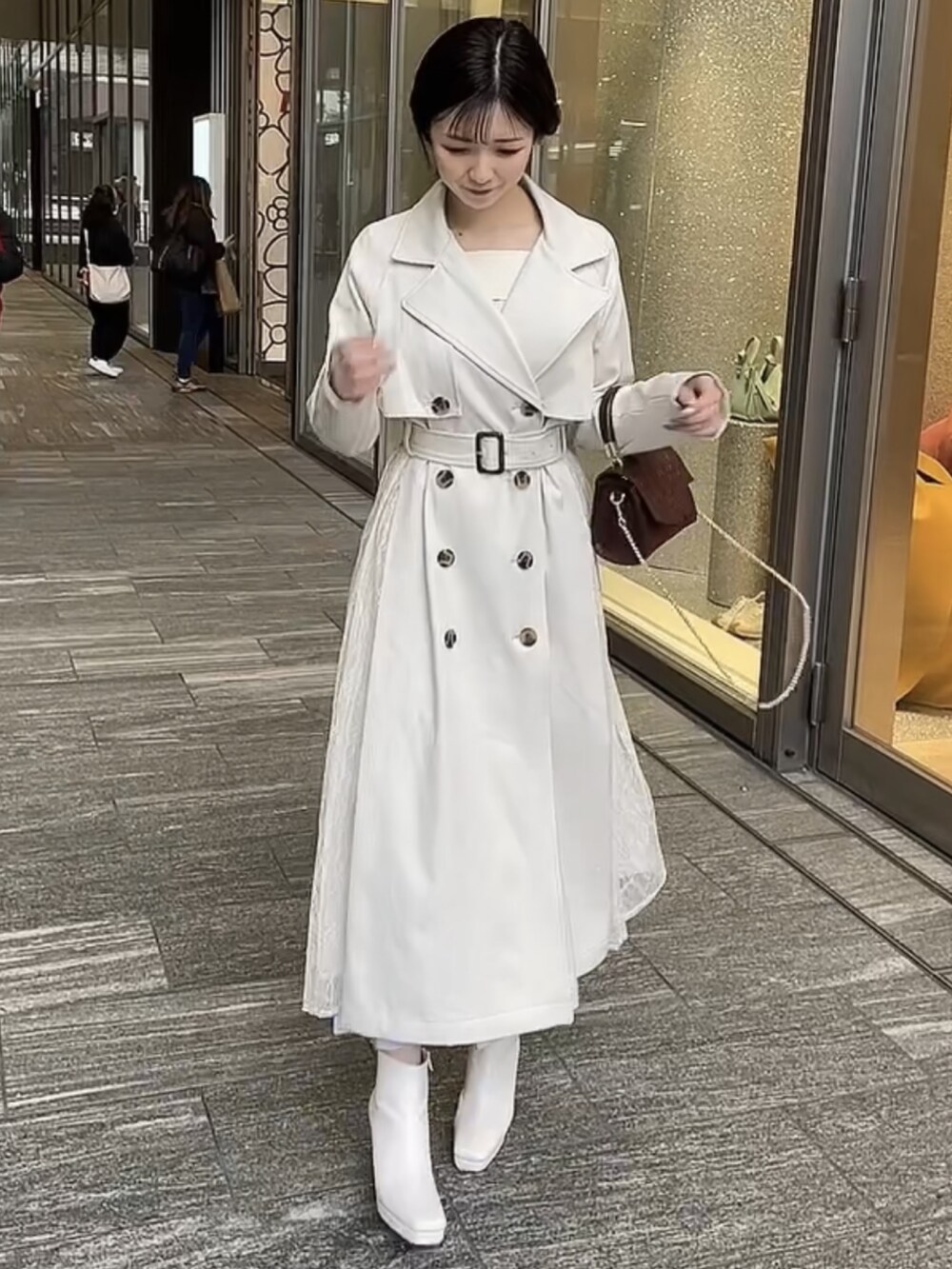 ブラウン系のハンドバッグ、ホワイト系のトレンチコート、ホワイト系のブーツを着用したレディースの冬コーディネートの3枚目の写真