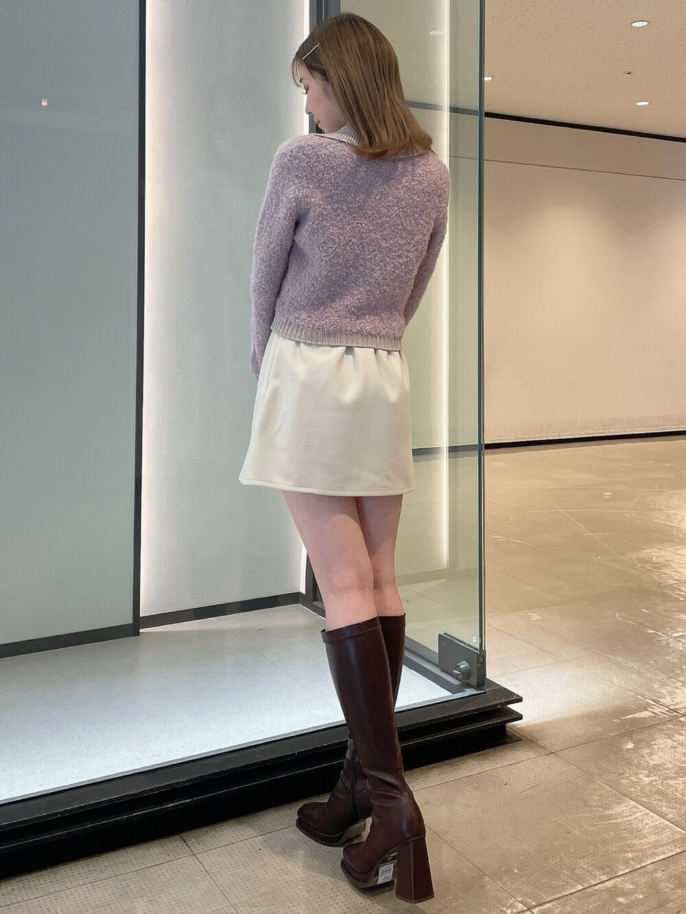 パープル系のニット/セーター、ホワイト系のスカート、ブラウン系のブーツを着用したレディースの冬コーディネートの3枚目の写真