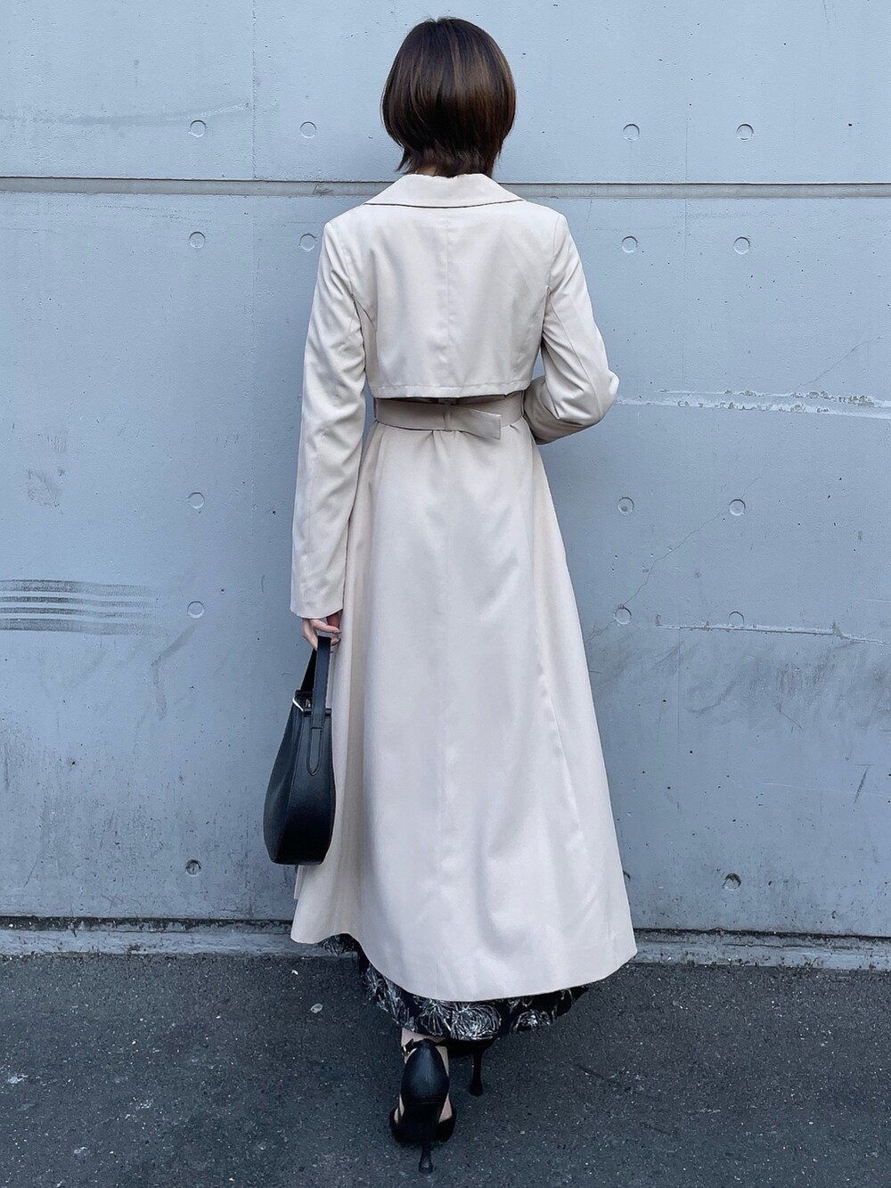 ベージュ系のトレンチコート、ブラック系のワンピース、ブラック系のハンドバッグを着用したレディースの冬コーディネートの7枚目の写真