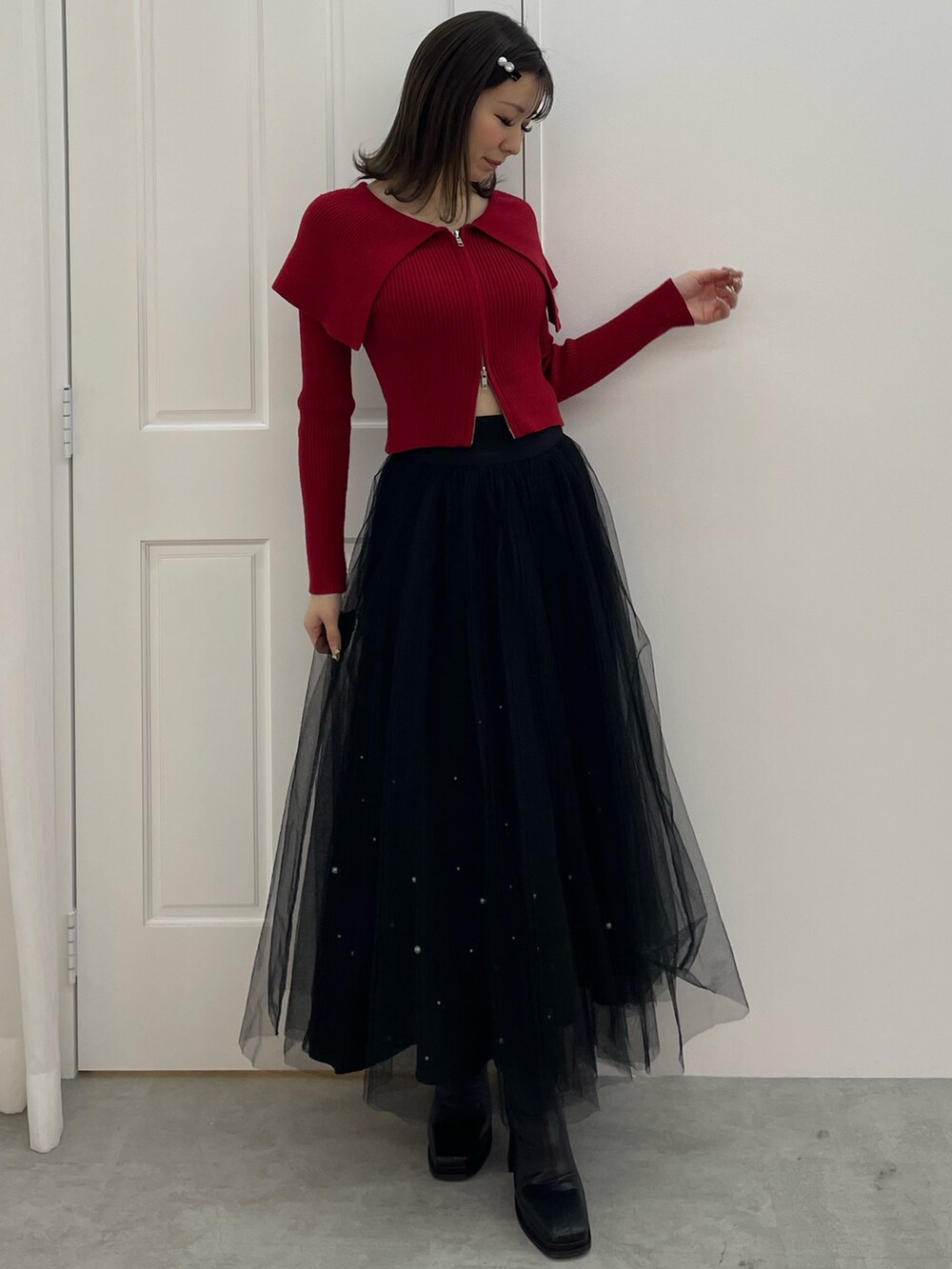 レッド系のニット/セーター、ブラック系のスカート、ブラック系のブーツを着用したレディースの秋コーディネートの2枚目の写真