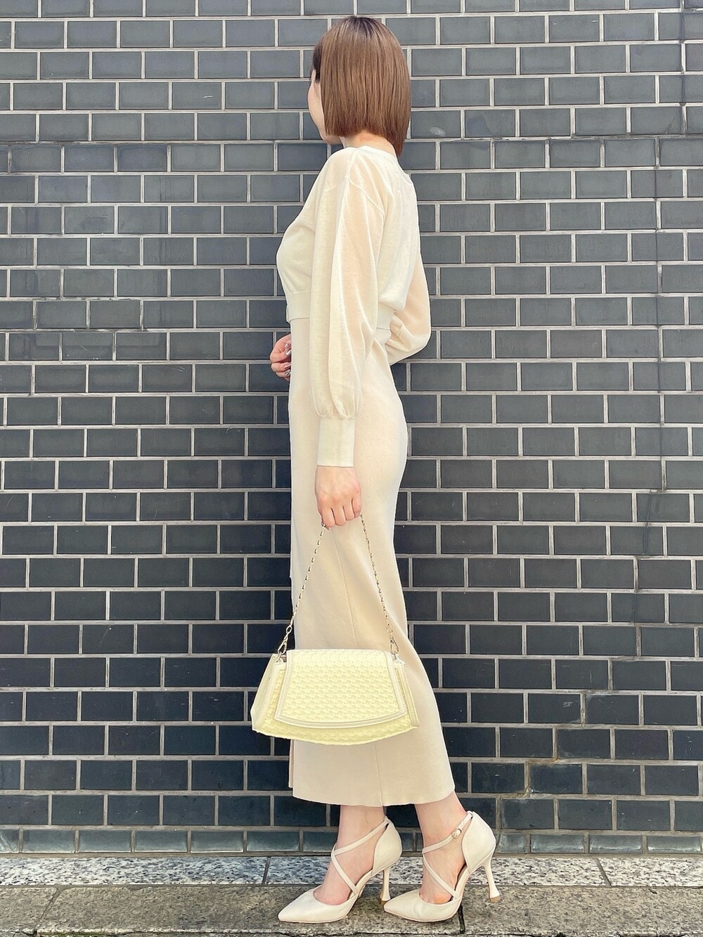 イエロー系のハンドバッグ、ホワイト系のパンプス、イエロー系のワンピースを着用したレディースの春コーディネートの3枚目の写真