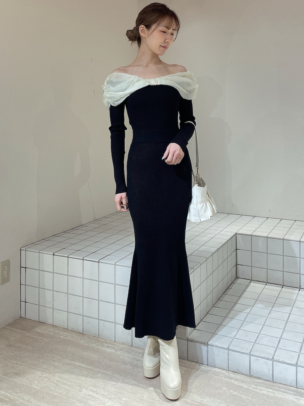 ホワイト系のハンドバッグ、ホワイト系のブーツ、ブラック系のワンピースを着用したレディースの冬コーディネートの2枚目の写真