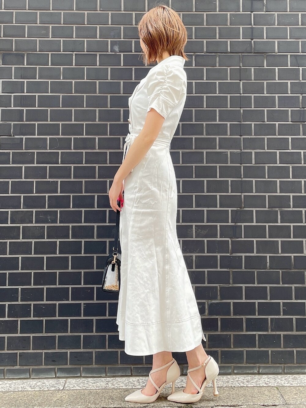 ホワイト系のワンピース、ブラック系のハンドバッグ、ホワイト系のパンプスを着用したレディースの春コーディネートの2枚目の写真