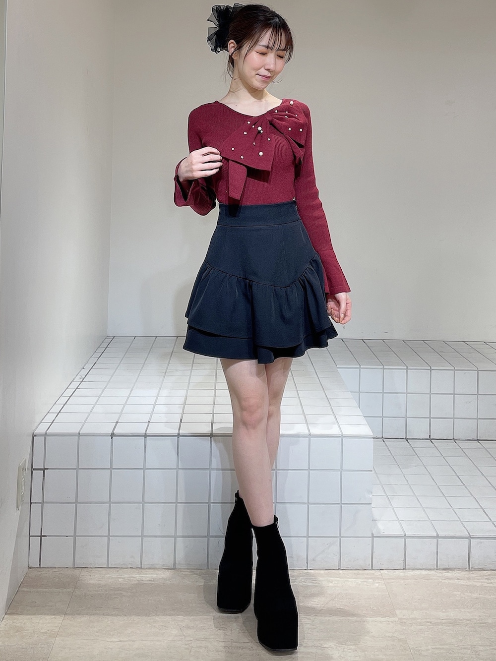 レッド系のニット/セーター、ブラック系のスカート、ブラック系のブーツを着用したレディースの冬コーディネートの2枚目の写真