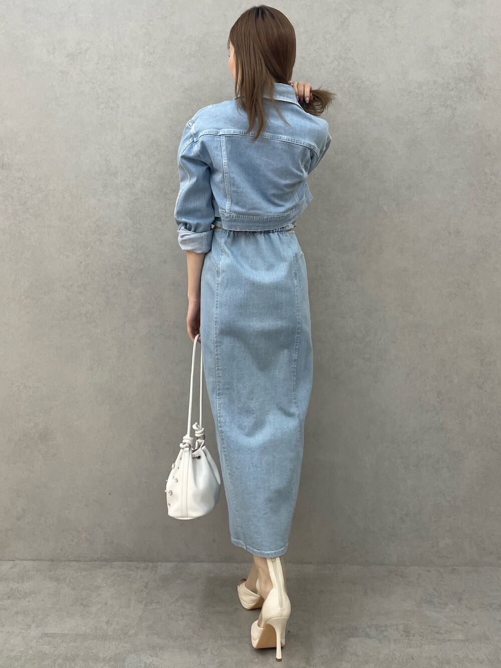 ブルー系のデニムジャケット、ブルー系のワンピース、ホワイト系のハンドバッグを着用したレディースの春コーディネートの3枚目の写真