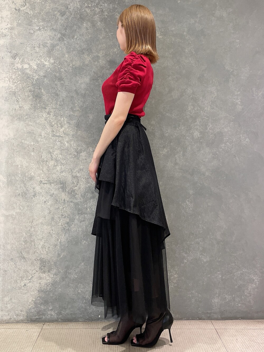 レッド系のニット/セーター、ブラック系のデニムスカート、ブラック系のブーツを着用したレディースの夏コーディネートの3枚目の写真