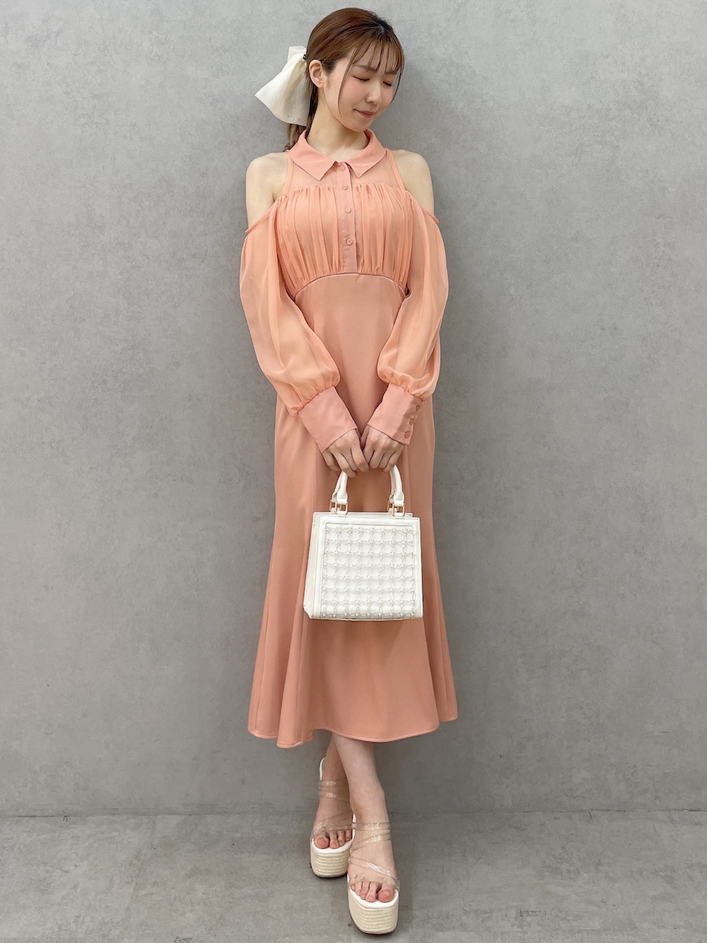 オレンジ系のワンピース、ホワイト系のハンドバッグ、ホワイト系のサンダルを着用したレディースの春コーディネートの2枚目の写真