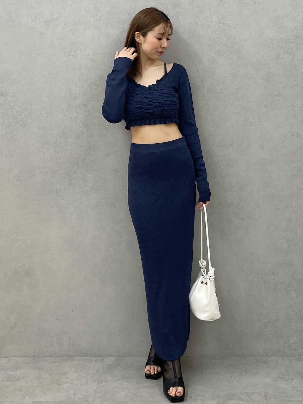 ブルー系のニット/セーター、ブルー系のスカート、ホワイト系のハンドバッグを着用したレディースの春コーディネートの2枚目の写真