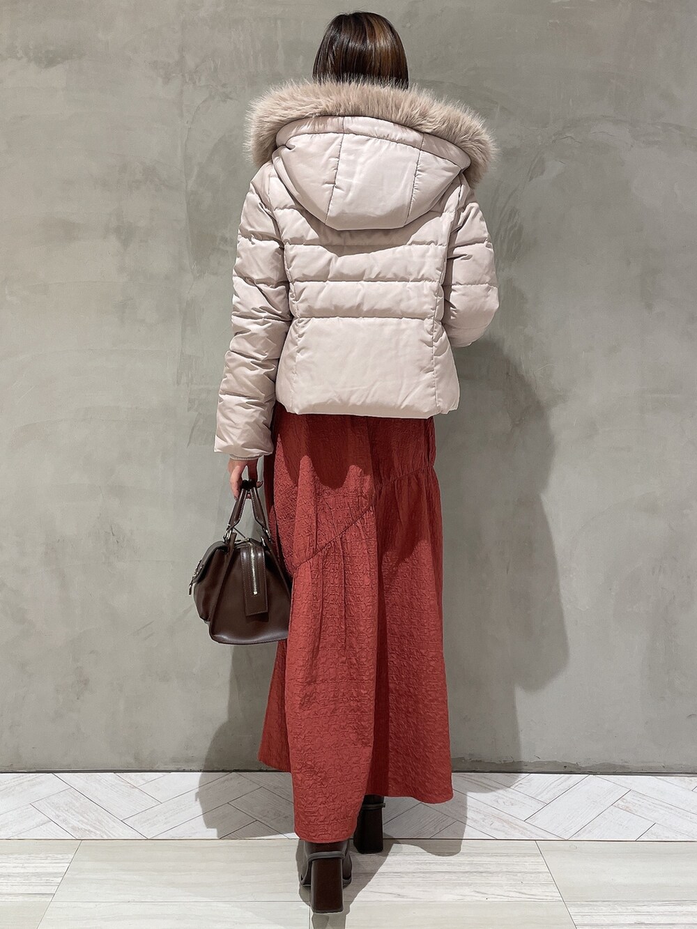 ベージュ系のダウンジャケット/コート、ブラック系のニット/セーター、ブラウン系のハンドバッグを着用したレディースの秋コーディネートの3枚目の写真