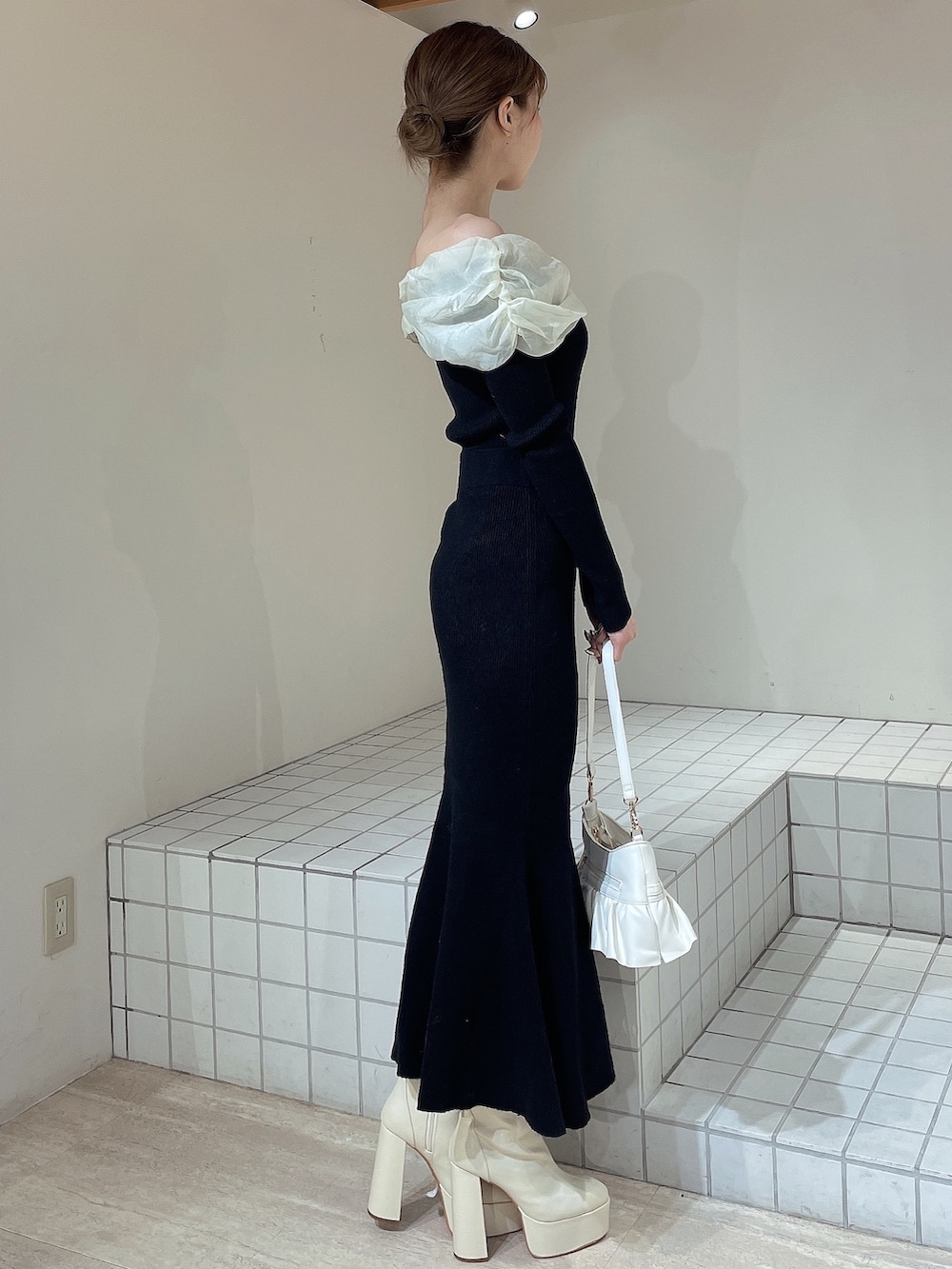 ホワイト系のハンドバッグ、ホワイト系のブーツ、ブラック系のワンピースを着用したレディースの冬コーディネートの3枚目の写真