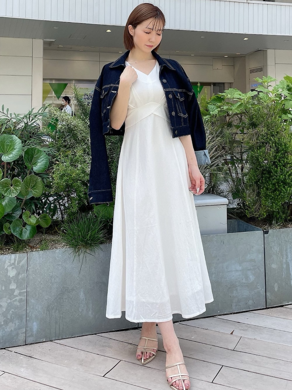ホワイト系のワンピース、ブルー系のデニムジャケット、ゴールド系のサンダルを着用したレディースの春コーディネートの2枚目の写真